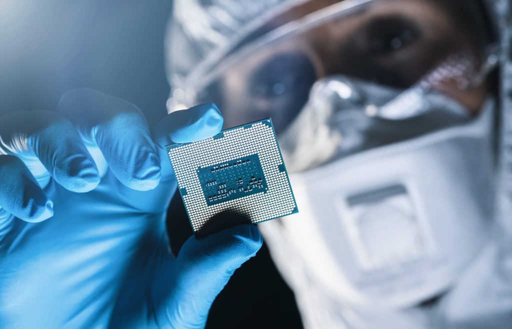 Photo: Utra Modern Electronic Manufacturing Factory, Engineer in Sterile Coverall Holds Microchip with Gloves and Examines it. Credit: rcphotostock / Alamy Stock Photo
