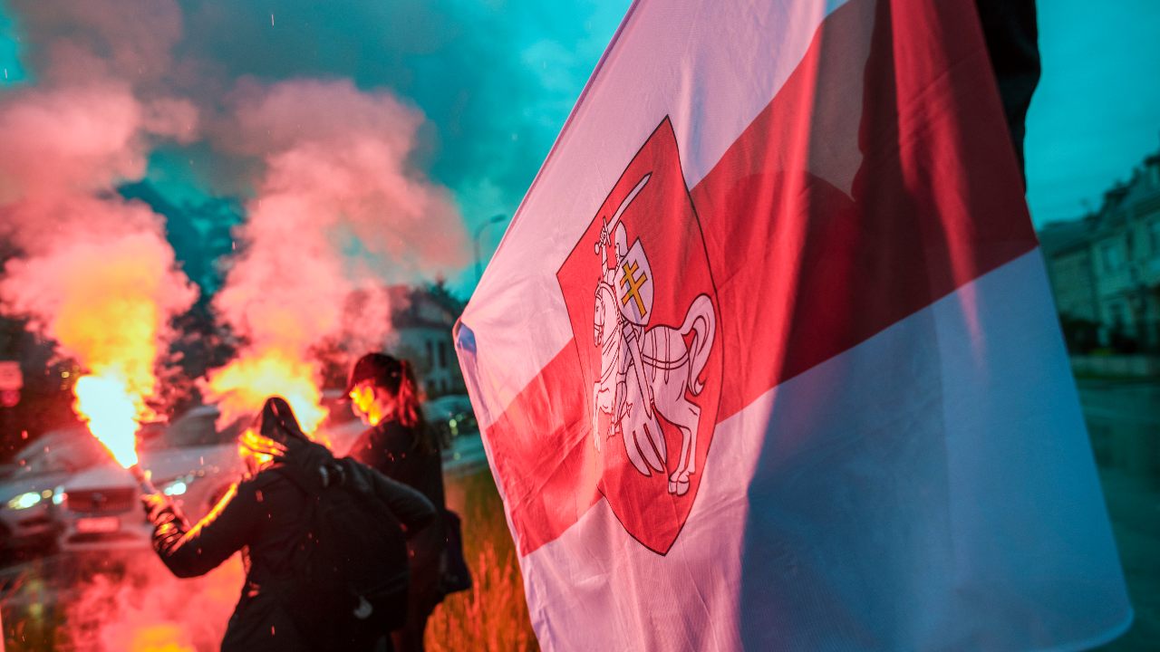 Photo: Protesters burn flares and wave the forbidden historical Belarusian flag during the protest. Belarusians residents in Poland gathered outside the Embassy of Belarus to protest against the arrest of Roman Protesevich, dissident journalist and the repressions on activists by Aleksander Lukashenko. Credit: Attila Husejnow / SOPA Images/Sipa USA