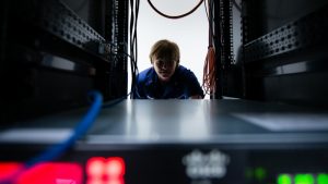 Photo: U.S. Coast Guard Chief Warrant Officer DeAnna Melleby, Information Systems Security Officer for the Coast Guard Command, Control, Communication and Information Technology unit at Coast Guard Base Boston, peers through a space in a server April 20, 2017. Melleby and her team have a number countermeasures they use to keep the Coast Guard computer network secure, including a 'sniffer' program that identifies when USBs or cell phones are plugged into the system. Credit: U.S. Coast Guard photo by Petty Officer 3rd Class Andrew Barresi