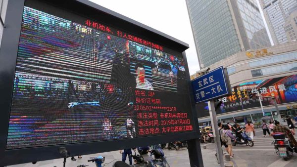 Photo: Pedestrians walk across a crossroad as a big electronic screen supported by face-recognition system shows the image of a jaywalker at the intersection in Nanjing city, east China's Jiangsu province, 4 July 2019. Traffic police in Nanjing used facial-recognition technology to capture jaywalkers in east China's Jiangsu province. Authorities already publicly name and shame people who flout the southern city’s strict road rules, using CCTV cameras equipped with artificial intelligence (AI) that can recognise offenders. Credit: Wang Feng, Oriental Image