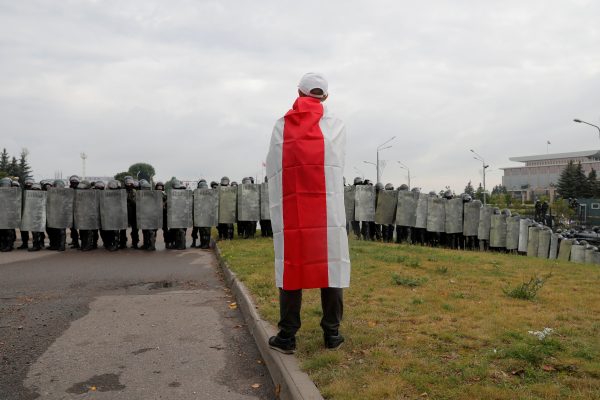 Photo: A man wearing a historical white-red-white flag of Belarus stands in front of law enforcement officers blocking a street during an opposition demonstration to protest against presidential election results, in front of the Independence Palace in Minsk, Belarus August 23, 2020. Credit: REUTERS/Vasily Fedosenko