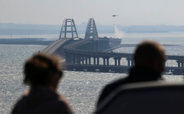 Photo: People watch fuel tanks ablaze on the Kerch bridge in the Kerch Strait, Crimea, October 8, 2022. Credit: REUTERS/Stringer