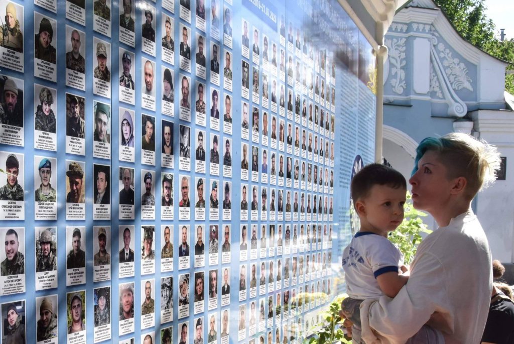 Photo: Lera Burlakova (author) and her son near the Wall of Remembrance of The Fallen in Kyiv, looking at pictures of my friends. Credit: Olena Khudiakova, a photojournalist and a soldier. 