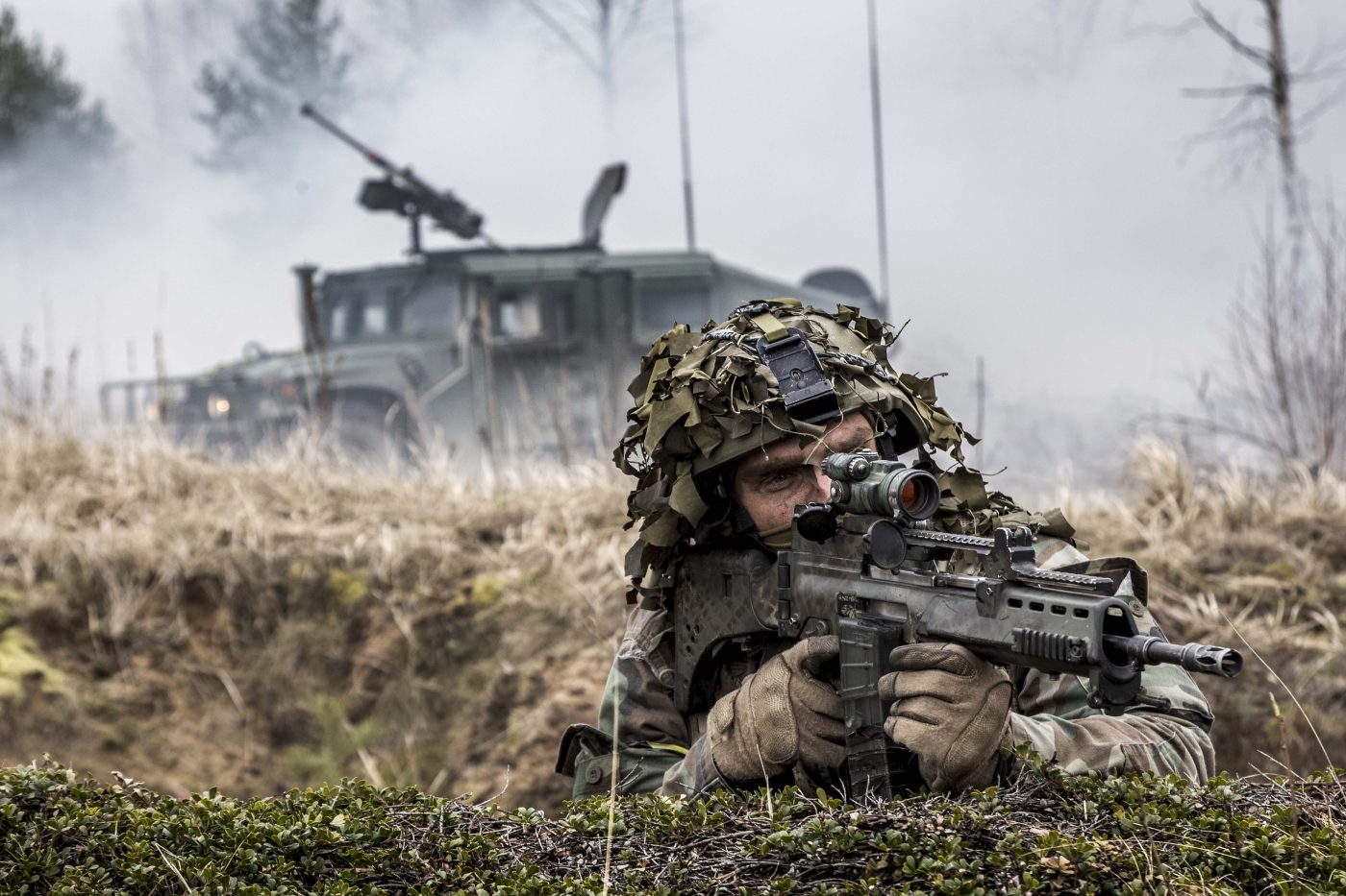 Photo: NATO Latvian soldier looks down the barrel of his weapon with a Humvee for protection in the background. Credit: Miks Užansfor NATO via Flickr. https://flic.kr/p/rda9VP