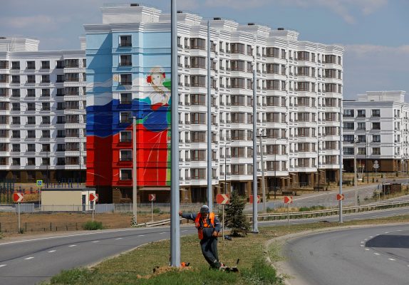 Photo: A worker takes a pause while mowing the grass in front of newly built apartment blocks, in the course of Russia-Ukraine conflict, in Mariupol, Russian-controlled Ukraine, August 16, 2023. Credit: REUTERS/Alexander Ermochenko
