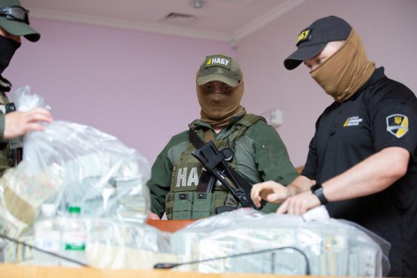 Photo: Officers stand next to plastic bags filled with US Dollar banknotes seized by the National Anti-Corruption Bureau of Ukraine, before a news briefing at the anti-corruption prosecutor's office in Kyiv, Ukraine June 13, 2020. According to the National Anti-Corruption Bureau of Ukraine, some $5 million was offered to anti-corruption officials and a further $1 million was intended for an official acting as a middleman. Credit: Press Service of the National Anti-Corruption Bureau of Ukraine/Handout via REUTERS