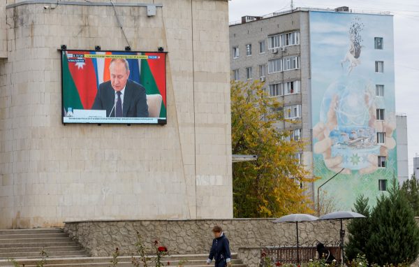 Photo: Russia's President Vladimir Putin is seen on a screen during the broadcast of a Russian state TV news report as a local resident walks near an apartment block decorated with a mural, an element of which depicts a nuclear power plant, in the course of Russia-Ukraine conflict in the city of Enerhodar in the Zaporizhzhia region, Russian-controlled Ukraine, October 14, 2022. Credit: REUTERS/Alexander Ermochenko