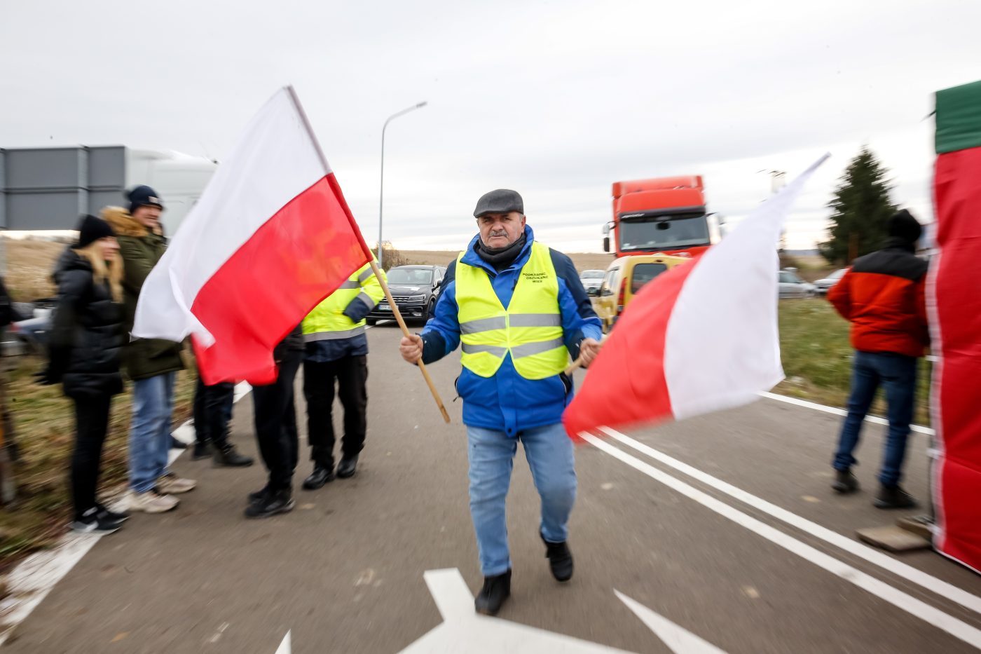 Photo: Polish farmer carries Polish flags on the strike post by the road as the farmers block truck transport in Medyka - another border crossing between Poland and Ukraine, on November 23, 2023. The farmers joined the transport sector in the strike against poor management of agricultural imports of Ukrainian produce as well as demand renegotiation of transport deals between Ukraine and the European Union. Medyka is the fourth strike site. Protesters already blocked 3 other crossings for truck transport, allowing only 4 trucks per an hour excluding humanitarian and military aid and sensitive chemical and food goods. According to the drivers, the queue to the Medyka crossing was nearly 7 days even before the strike started today. Credit: Dominika Zarzycka/NurPhoto.