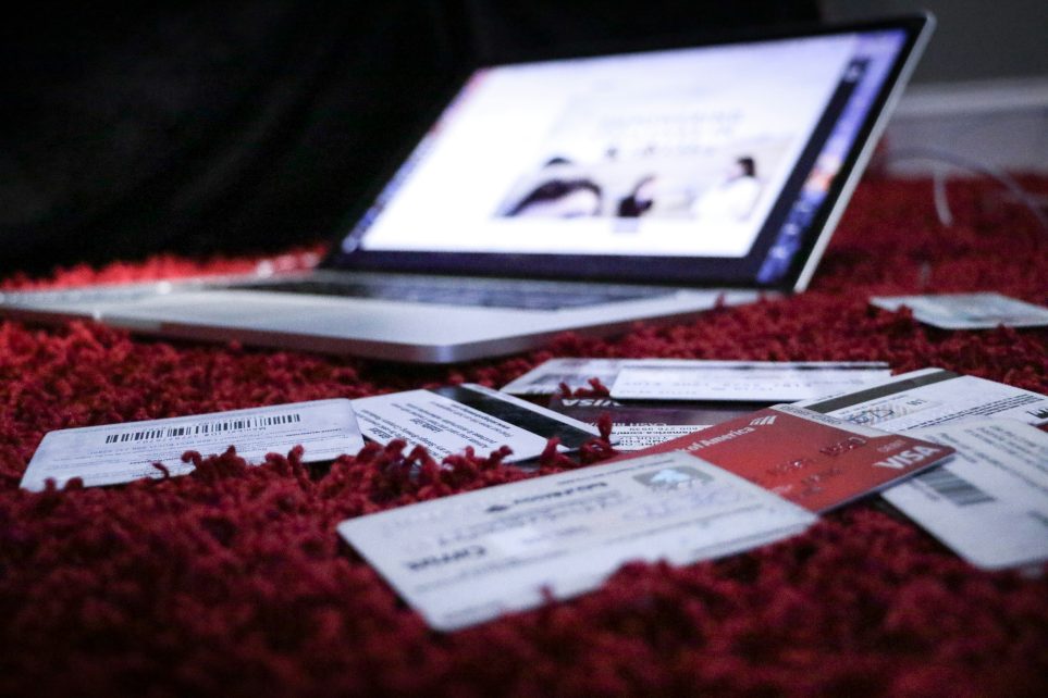 Photo: Credit cards scattered on a red carpet in front of an open laptop, symbolizing potential identity theft or online shopping. Credit: Dylan Gillis/Unsplash.