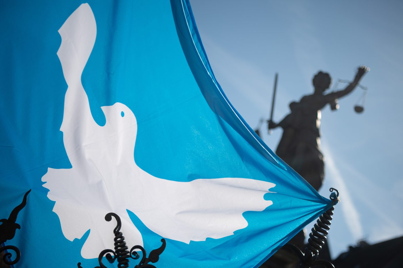 Photo: Ukraine war. A flag with a dove of peace hangs before the beginning of the final rally of the Easter march of the "Netzwerk Friedenskooperative" at the Fountain of Justice with the statue of Justitia, the goddess of justice with executioner's sword and scales. Under the slogan "Lay down your arms! Stop the war in Ukraine. Stop the 100-billion-euro rearmament program", several hundred participants took part in the Easter march. Credit: Sebastian Gollnow/dpa via Reuters Connect