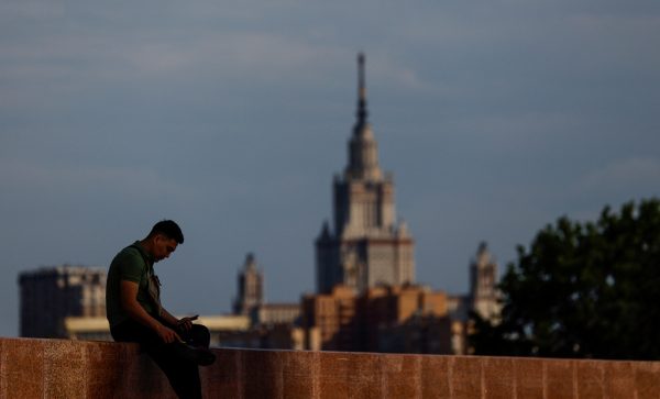 Photo: A man uses his mobile phone as he sits with the building of Moscow State University (MSU) in the background on a sunny day in Moscow, Russia June 26, 2023. Credit: REUTERS/Maxim Shemetov