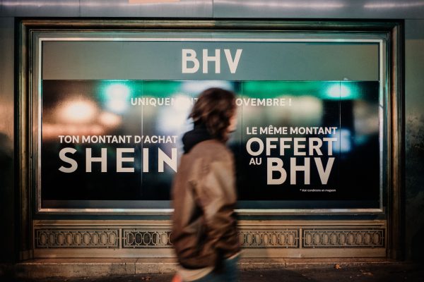 Photo: Illustration of a person walking in front of a poster on the BHV Bazar de l Hotel de Ville department store which reads BHV uniquement le 5 novembre ton montant d achat SHEIN le meme montant offert au BHV in Paris France on November 3, 2025. Credit: Reuters